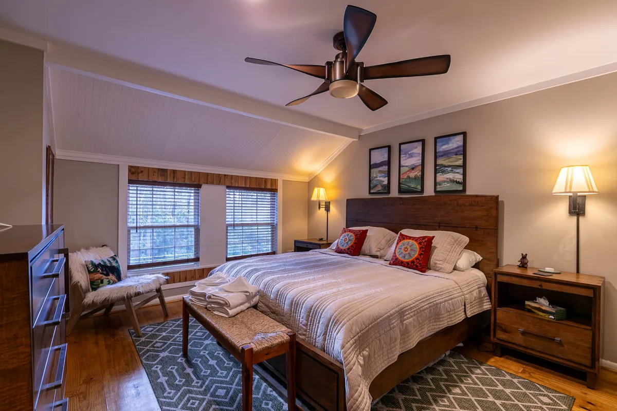 A tranquil bedroom featuring a plush bed, tasteful artwork, nightstands, and a window that brings in soft natural light. The overall mood is calm and inviting.