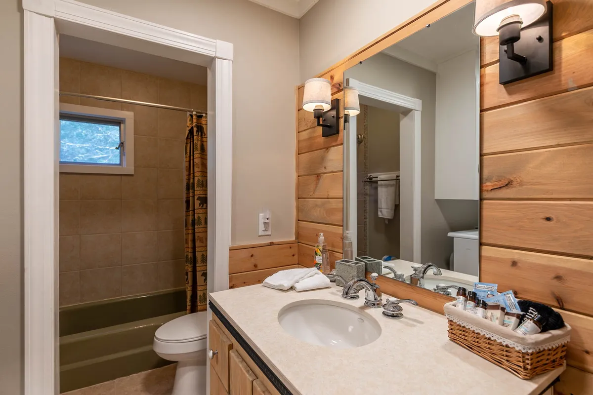 A cozy bathroom with a wooden vanity, large mirror, and plush towels on a rack. The space is well-lit, clean, and inviting, providing a perfect spot for refreshing or unwinding after an active day.