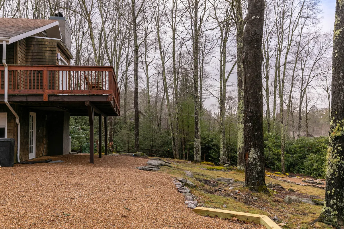 An exterior view of the deck surrounded by trees and a gravel area, offering a tranquil spot ideally suited for outdoor relaxation, wildlife watching, or hosting family gatherings. The expanse and wooded setting promote the idea of a safe, private space for children and adults alike.