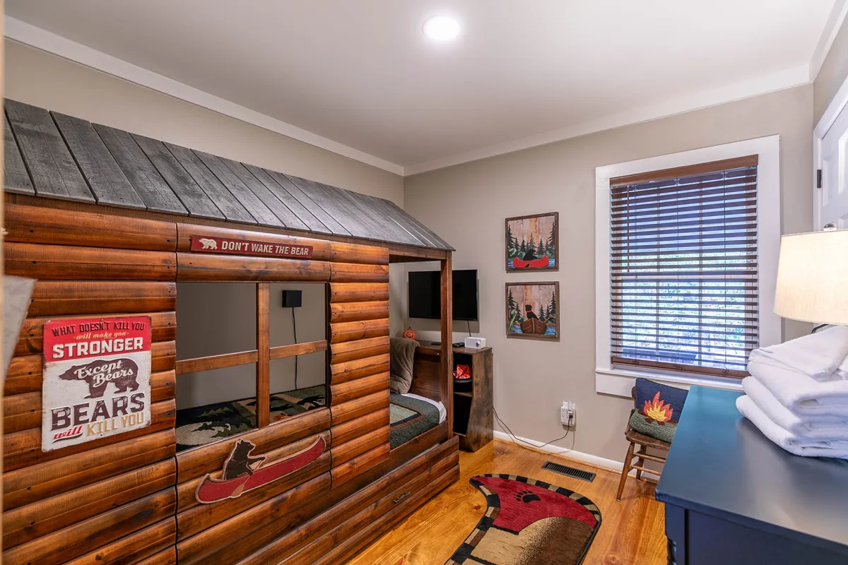 A whimsical bedroom featuring a bear-themed bed, wooden decor, and playful artwork on the walls. The room is inviting for children or families, encouraging imaginative play and cozy storytime moments.
