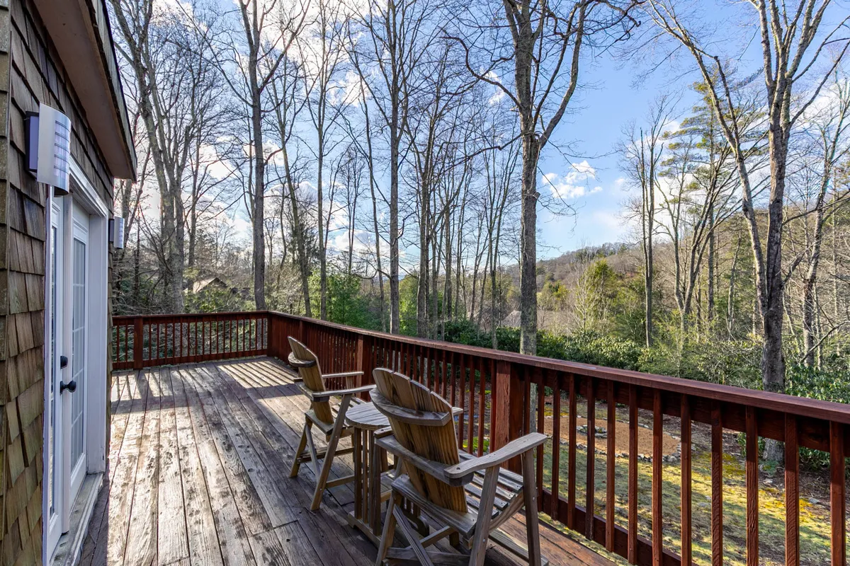 A serene wooden deck surrounded by lush trees, featuring comfortable seating arranged to take in the peaceful forest view. This space is ideal for relaxing, enjoying a morning coffee, or quietly connecting with nature, with hints of sunrise light filtering through the leaves.
